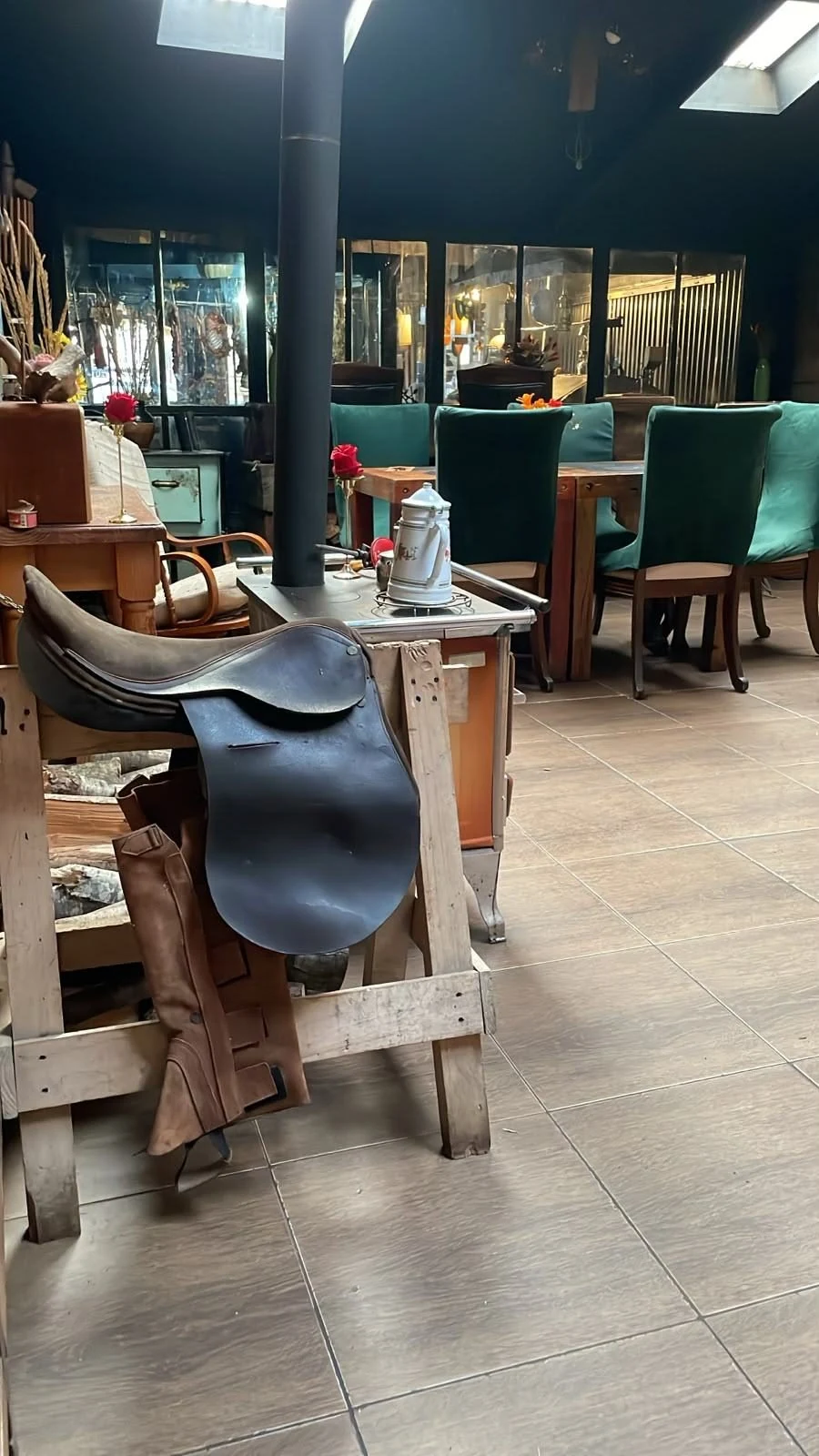 Silla de montar y botas de cuero junto a una mesa con sillas verdes