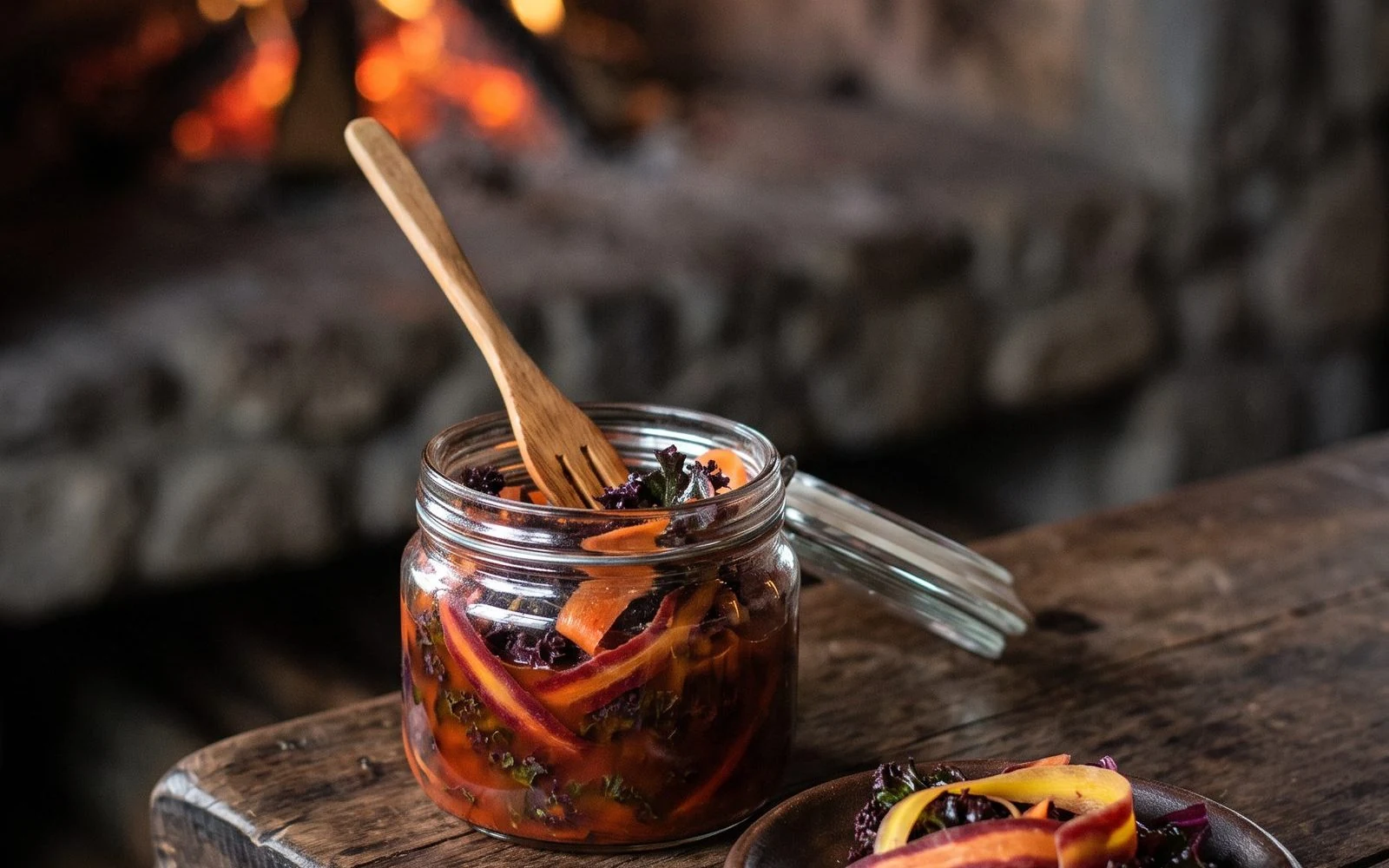 Glass jar of Patagonian kimchi made with purple kale and rainbow carrots, with a small dish beside it