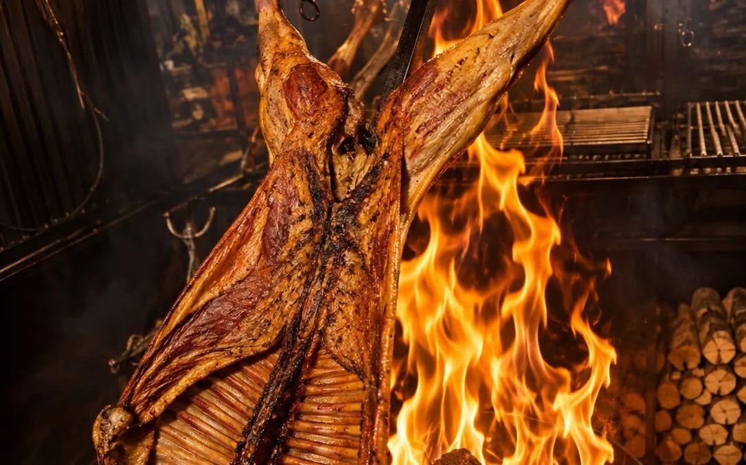 Magellanic lamb on the spit, opened on the iron cross in front of the wood flames
