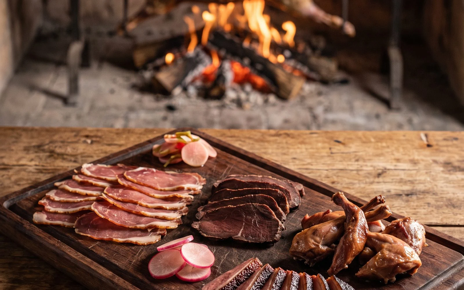 Steppe board: slices of cured wild boar leg, smoked guanaco, wild duck and rabbit, with lamb over the fire behind