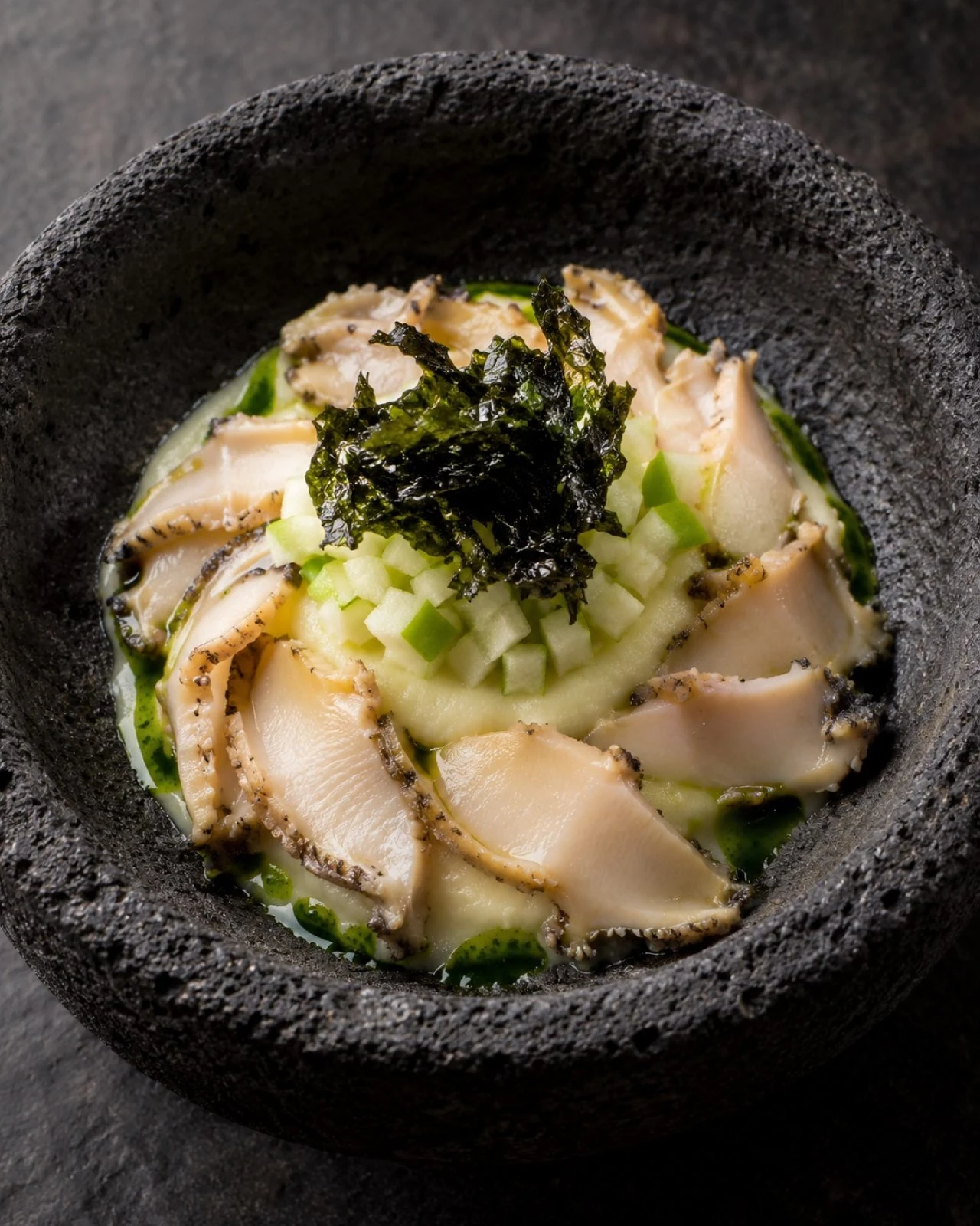 Sliced abalone on creamy potato with luche, in a stone bowl